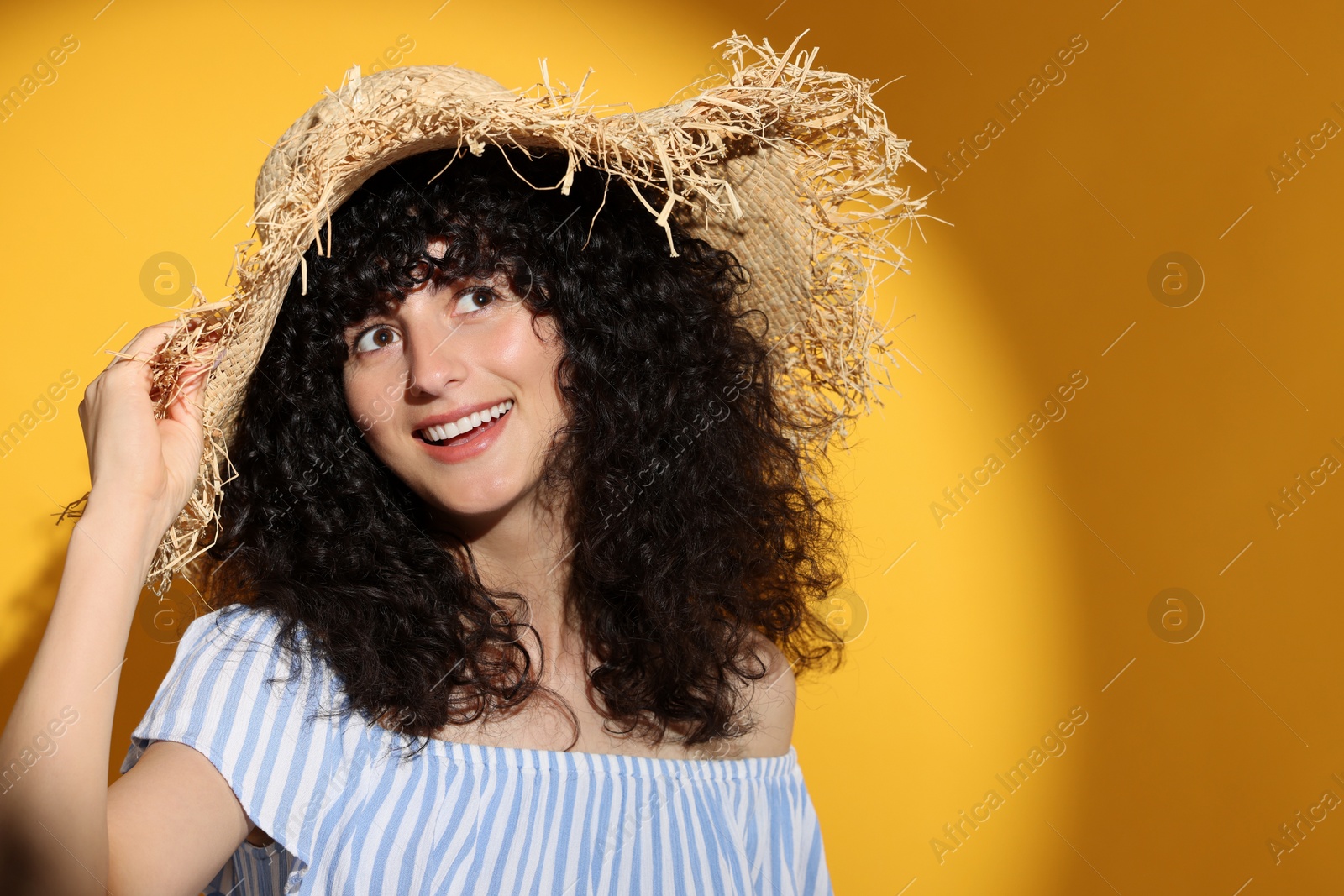 Photo of Beautiful young woman wearing straw hat in sunlight on orange background, space for text. Sun protection accessory