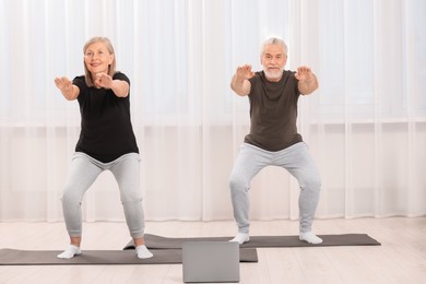 Photo of Senior couple practicing yoga with laptop at home