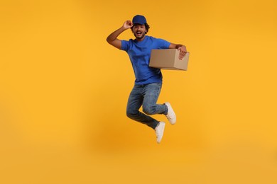 Photo of Happy courier with parcel jumping on orange background