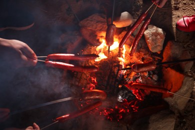 Photo of People roasting sausages on campfire outdoors at night, closeup