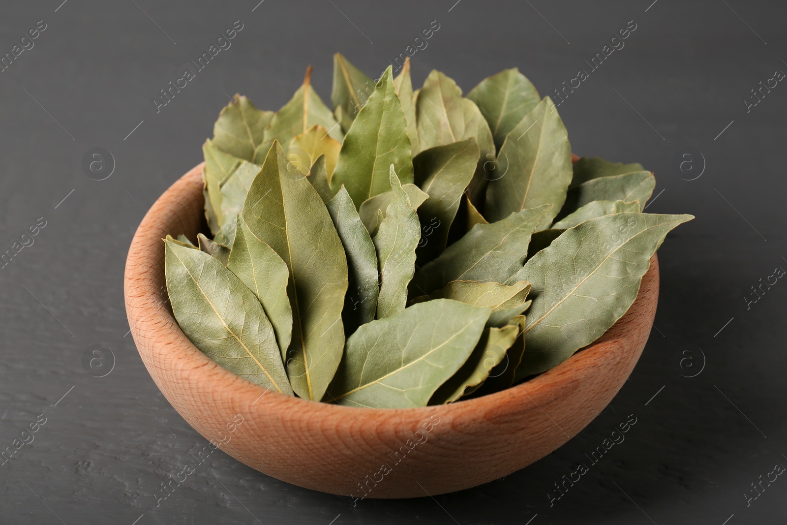 Photo of Aromatic bay leaves in wooden bowl on gray table