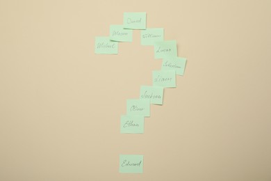 Photo of Choosing baby`s name. Paper stickers with different names in shape of question mark on beige background, top view