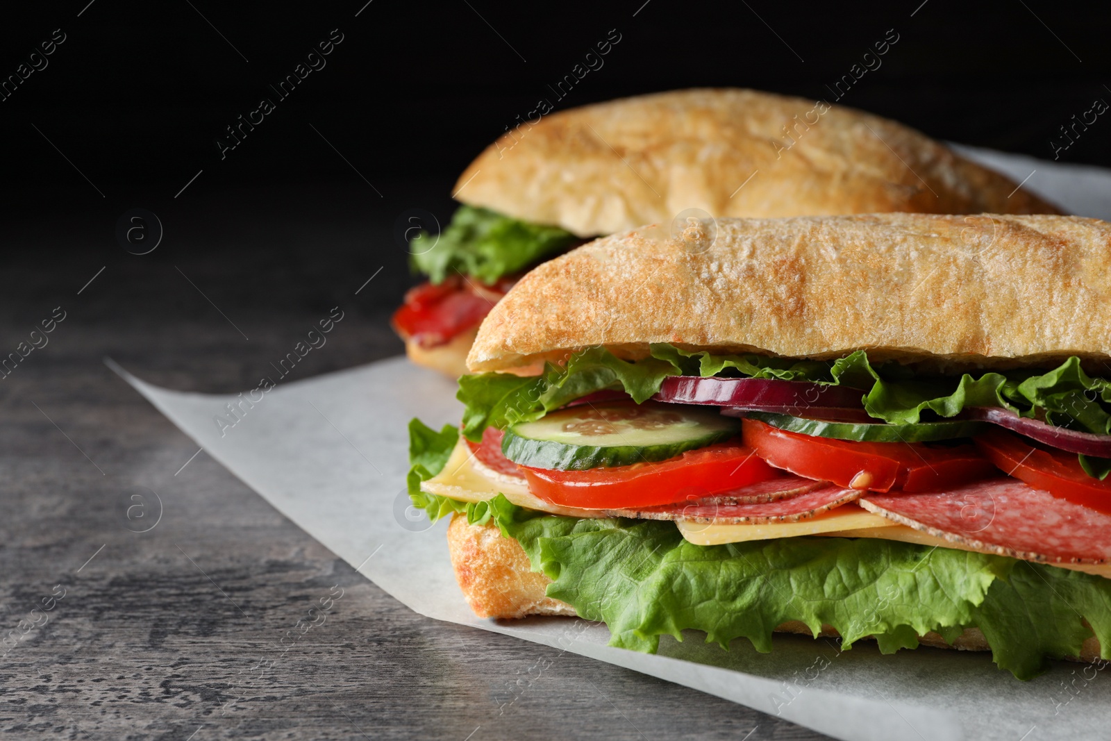Photo of Delicious sandwiches with fresh vegetables and salami on grey table, closeup