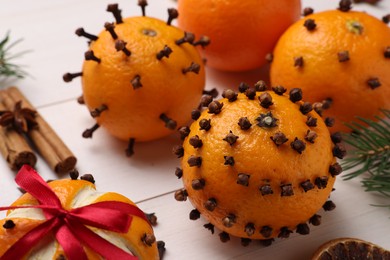 Photo of Pomander balls made of tangerines with cloves and fir branches on white wooden table, closeup