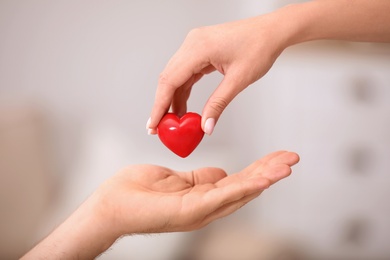 Woman giving red heart to man on blurred background, closeup. Donation concept