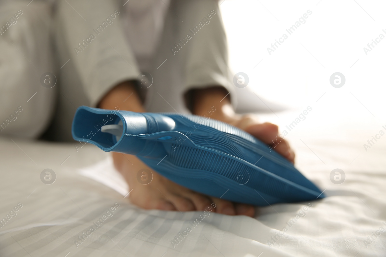 Photo of Man warming feet with hot water bottle on bed, closeup