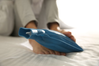 Photo of Man warming feet with hot water bottle on bed, closeup