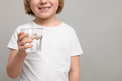 Photo of Little boy holding glass of fresh water on light grey background, closeup. Space for text