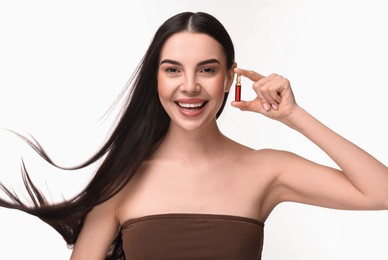 Beautiful young woman with long healthy hair holding ampoule on white background