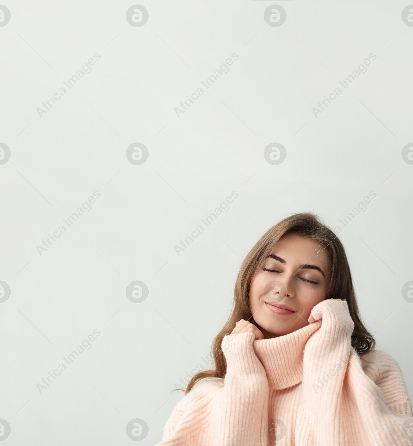 Photo of Beautiful young woman wearing warm pink sweater on light background. Space for text