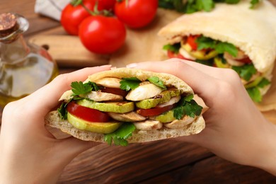 Woman holding delicious pita sandwich with grilled vegetables and parsley at wooden table, closeup