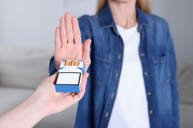 Woman refusing cigarettes on blurred background, closeup. Quitting smoking concept