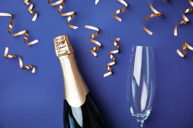 Photo of Christmas composition with bottle of champagne, glass and shiny streamers on color background, top view