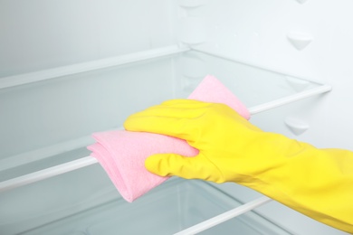 Woman cleaning empty refrigerator with rag, closeup