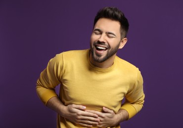 Photo of Young man laughing on purple background. Funny joke