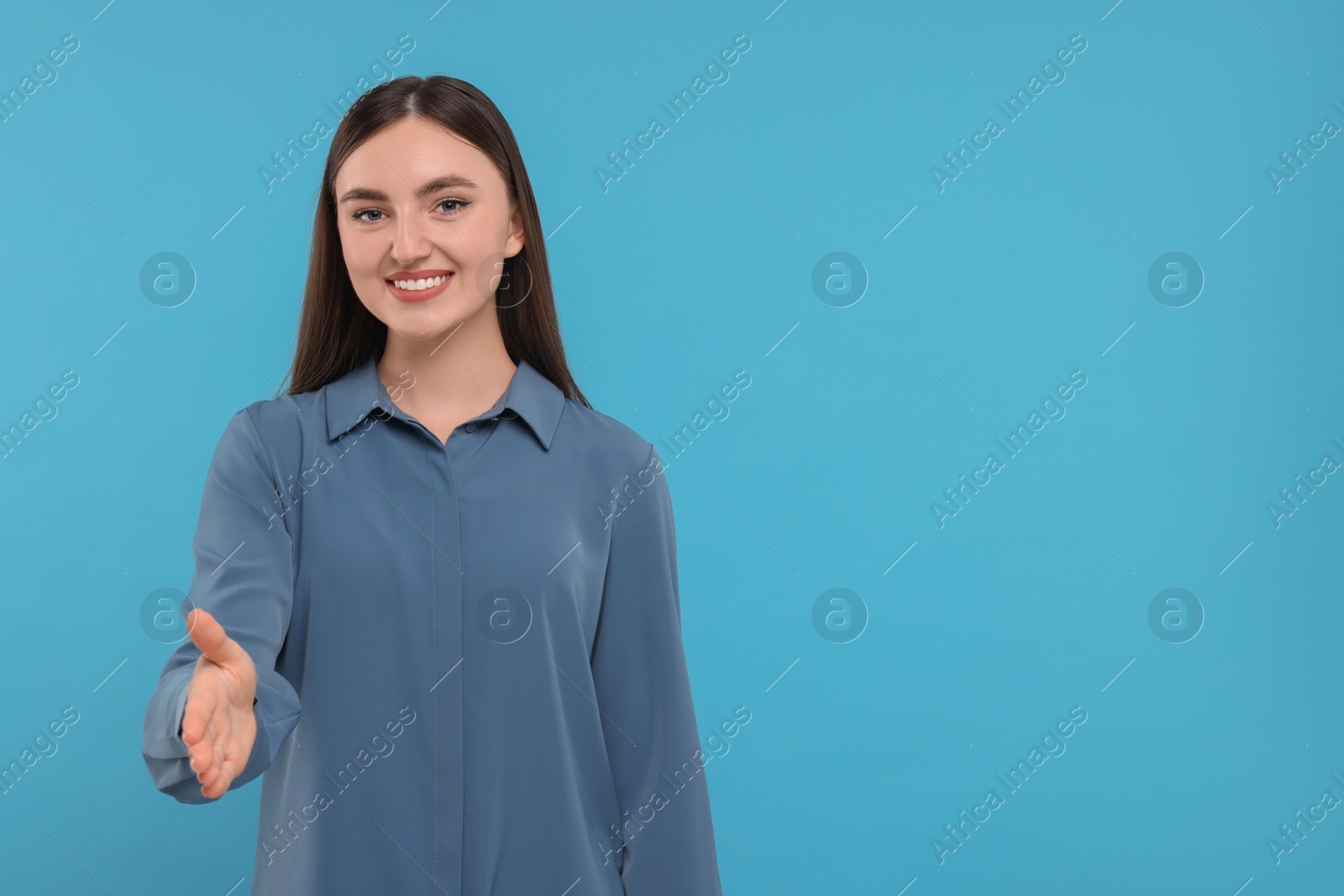 Photo of Smiling woman welcoming and offering handshake on light blue background. Space for text