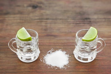 Photo of Mexican tequila shots with lime slices and salt on wooden table, space for text. Drink made from agave
