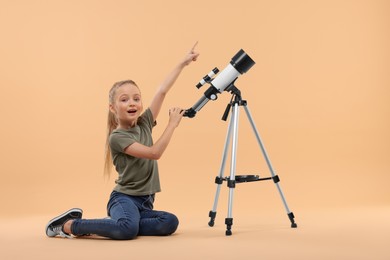 Photo of Excited little girl with telescope pointing at something on beige background, space for text