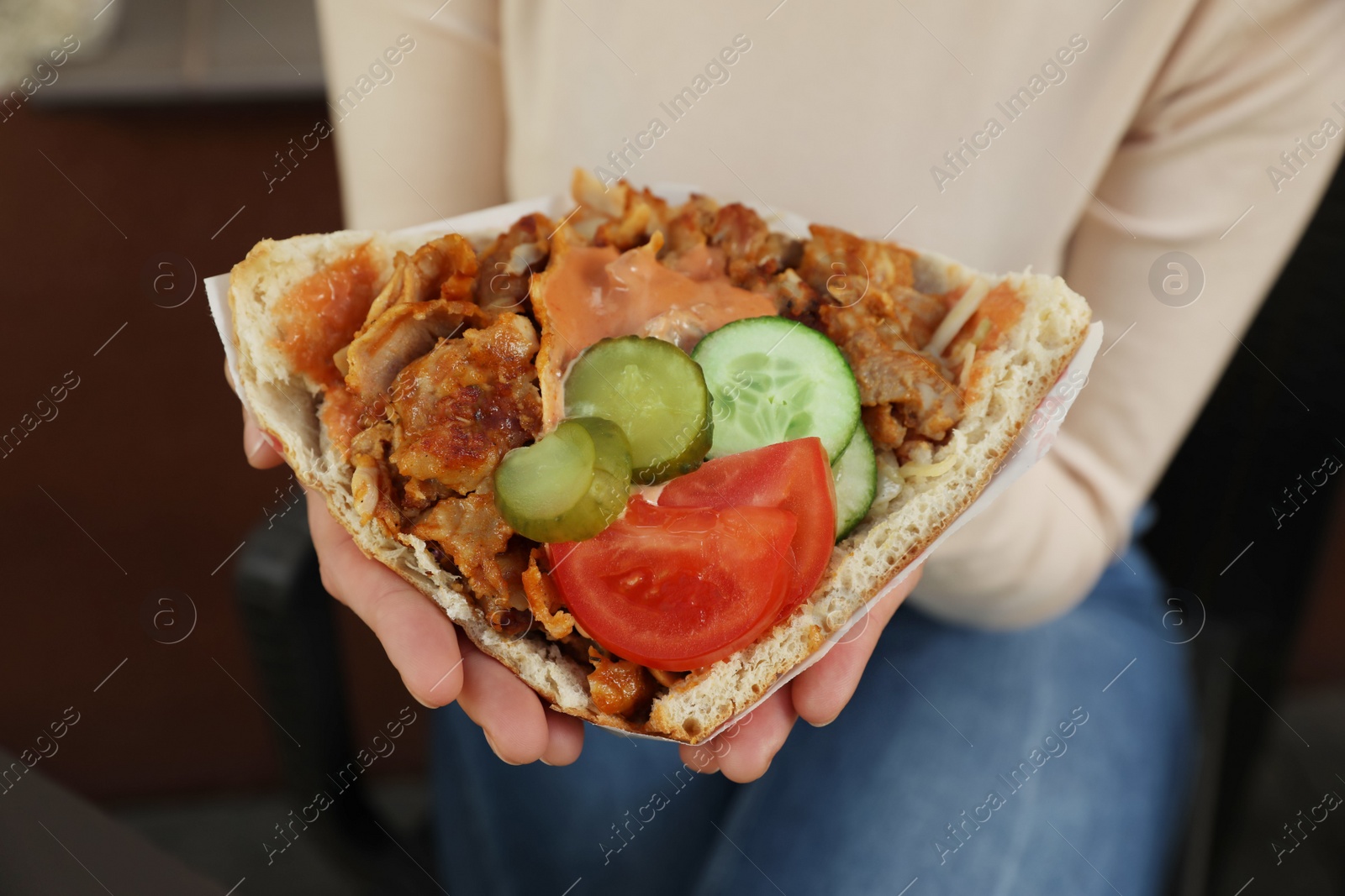 Photo of Woman holding delicious bread with roasted meat and vegetables indoors, closeup. Street food