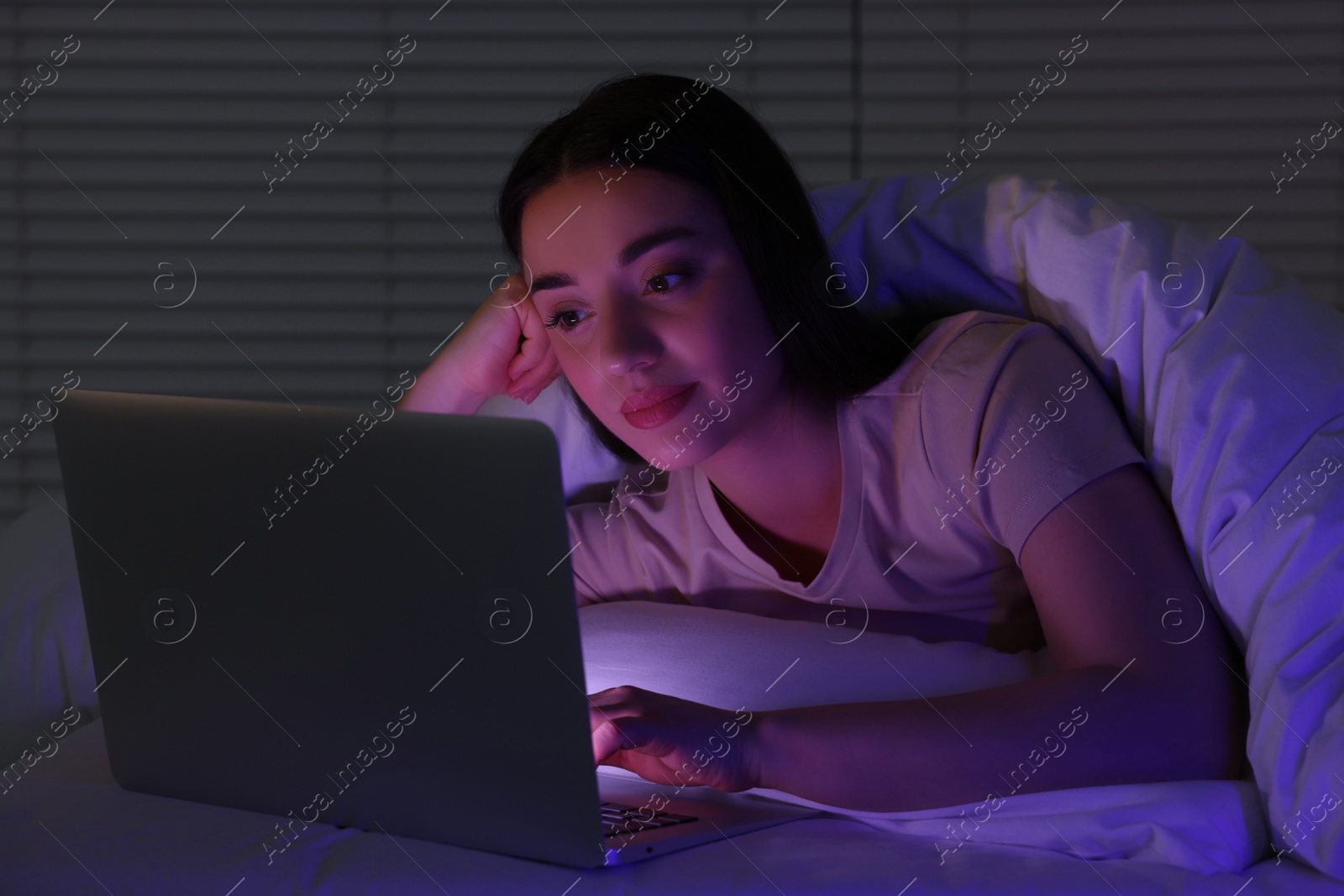 Photo of Young woman using laptop in bed at night. Internet addiction