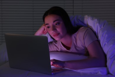 Young woman using laptop in bed at night. Internet addiction