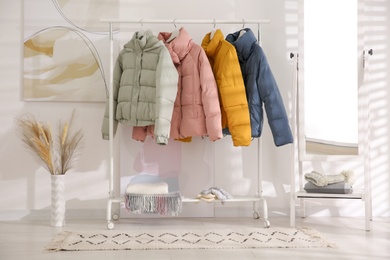 Photo of Different warm jackets on rack in stylish room interior