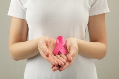 Woman with pink ribbon on light grey background, closeup. Breast cancer awareness