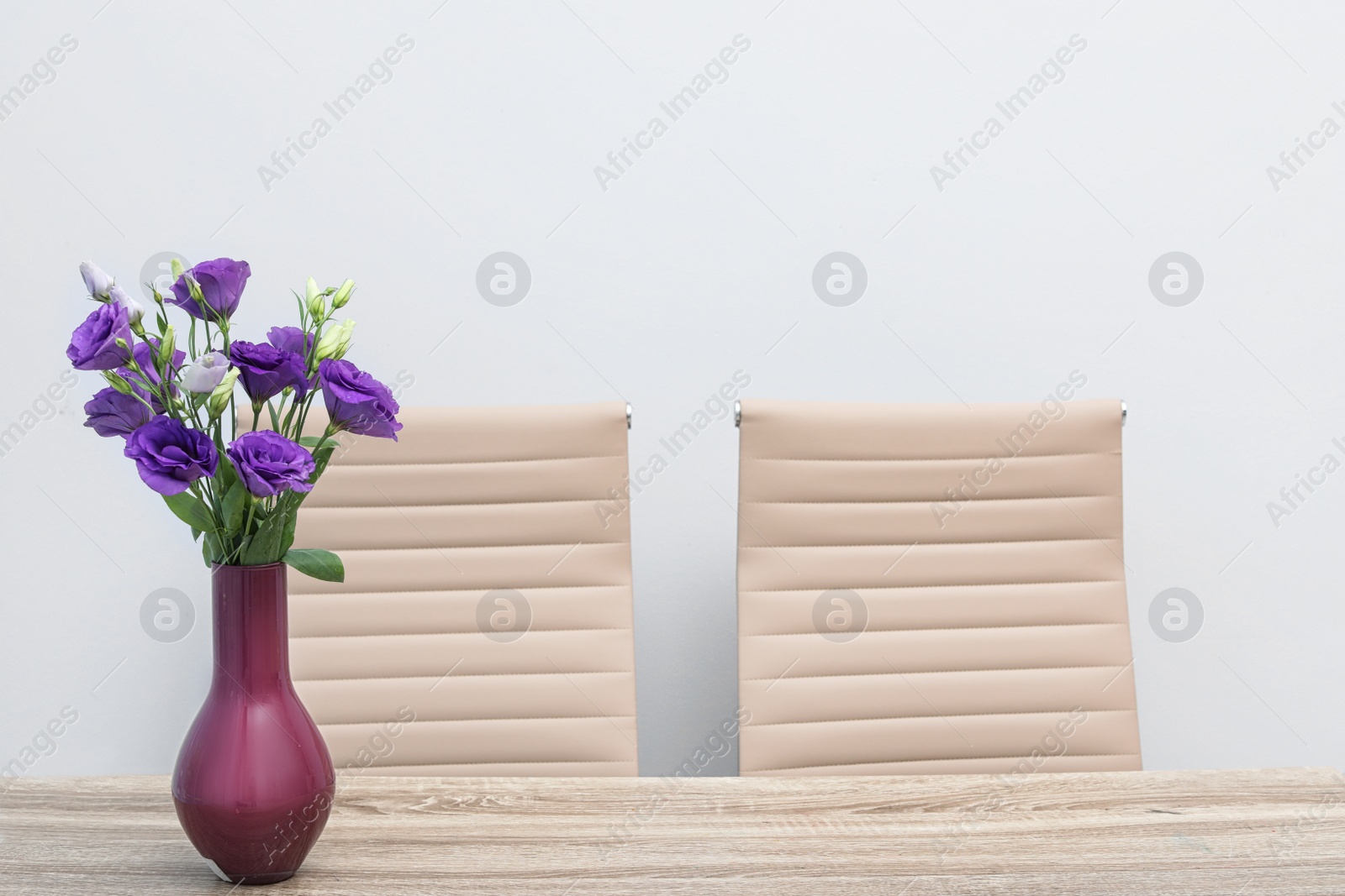 Photo of Beautiful bouquet in vase on wooden table against color background. Stylish interior