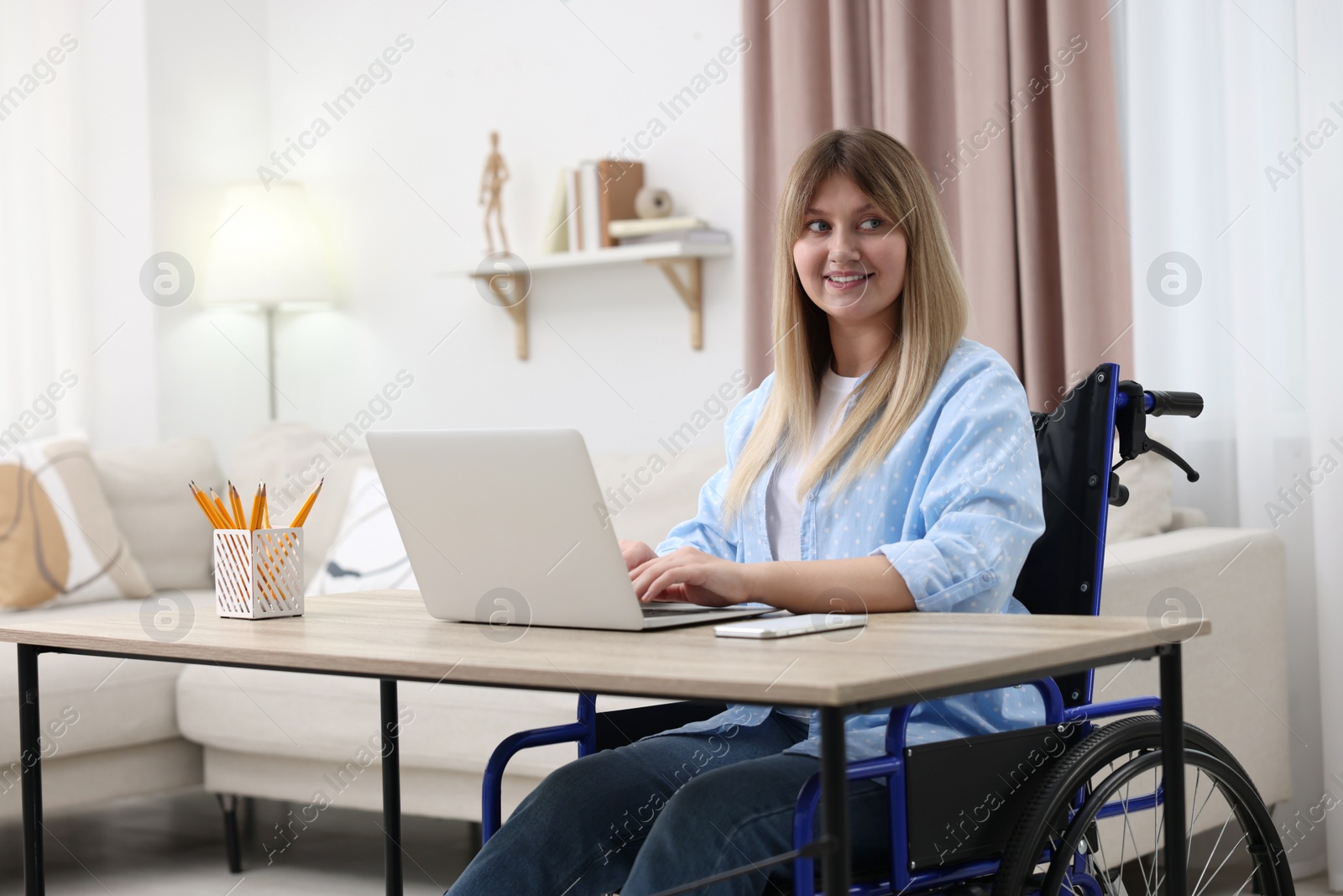 Photo of Woman in wheelchair using laptop at table in home office