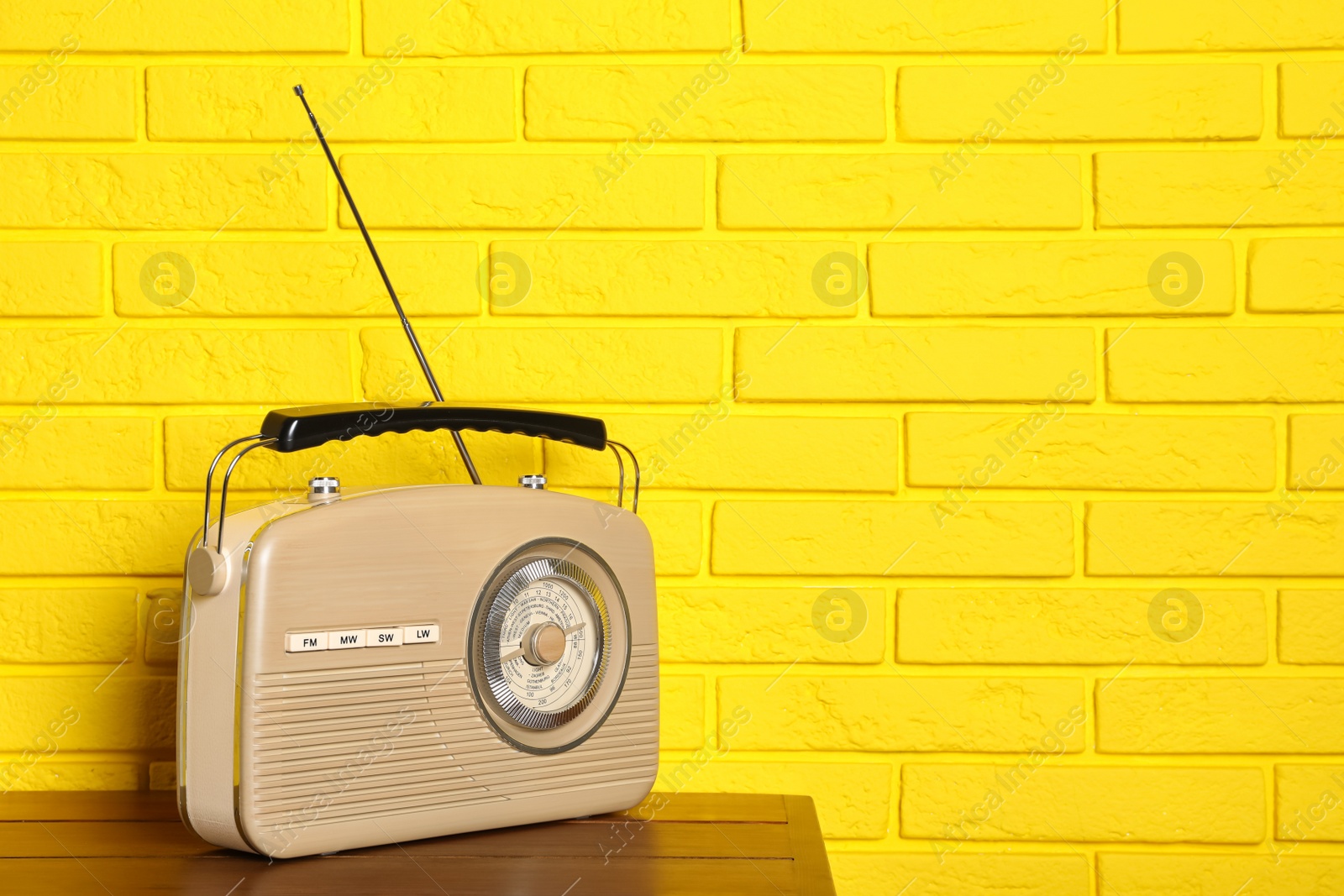 Photo of Retro radio receiver on wooden table near yellow brick wall. Space for text