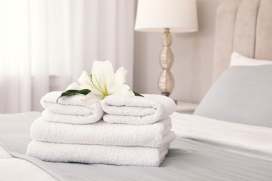 Photo of Stack of fresh towels with flower on bed indoors, space for text