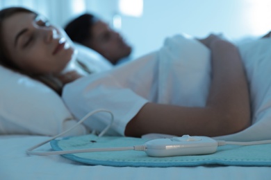 Couple sleeping in bed with electric heating pad, focus on cable