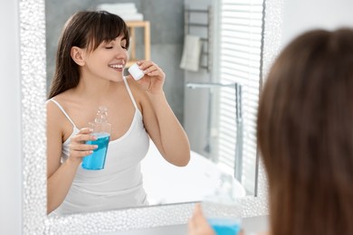 Young woman using mouthwash near mirror in bathroom