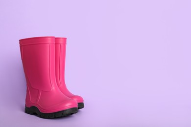 Photo of Bright pink rubber boots on violet background. Space for text
