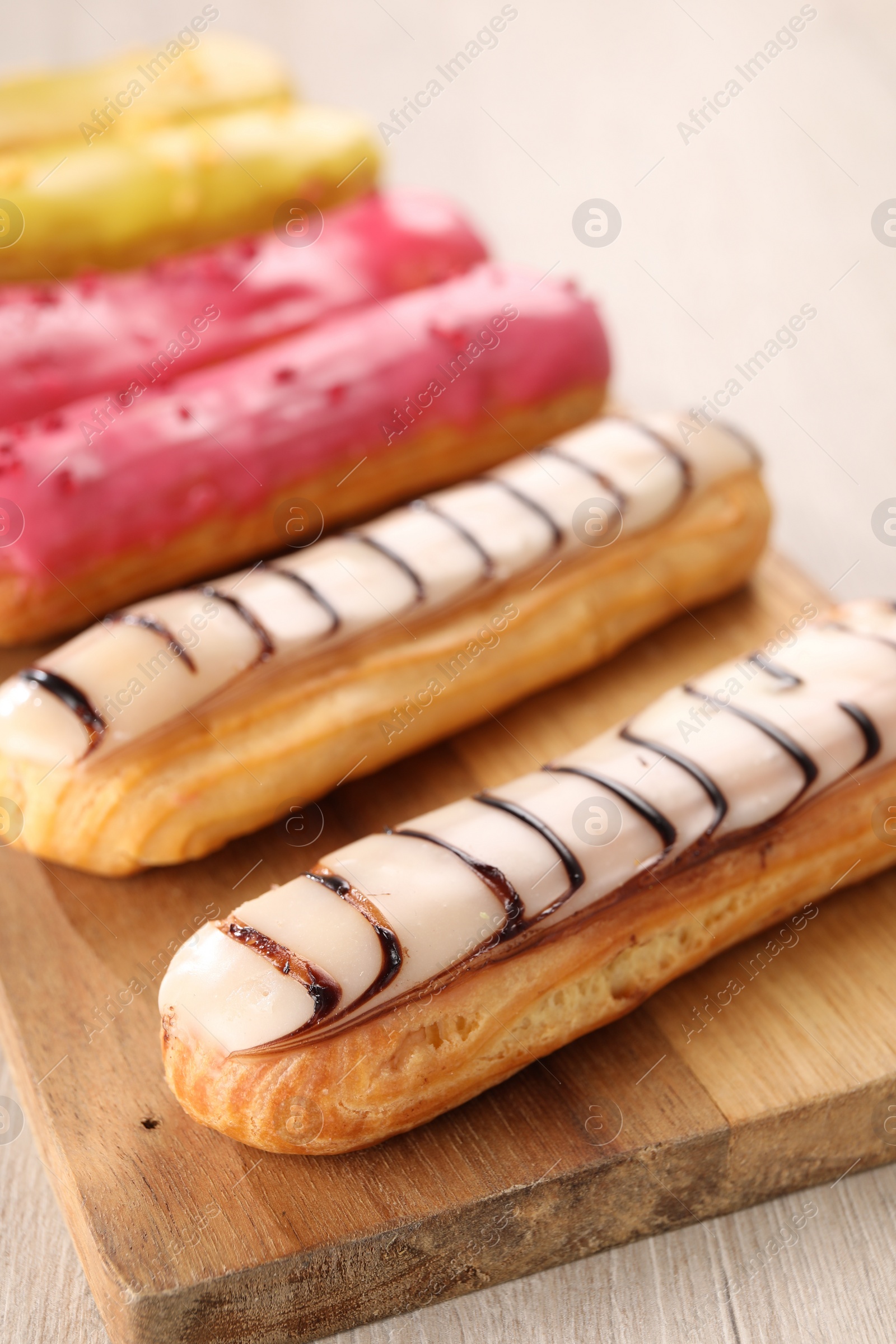 Photo of Board with different tasty glazed eclairs on light wooden table, closeup