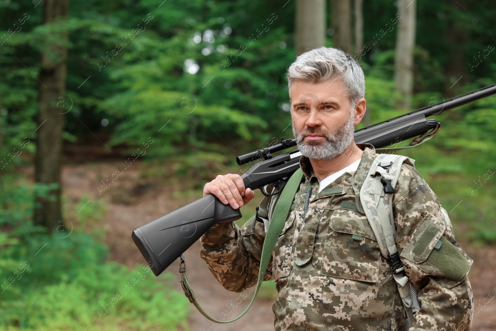 Photo of Man with hunting rifle wearing camouflage in forest. Space for text