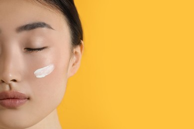 Photo of Beautiful young woman with sun protection cream on her face against orange background, closeup. Space for text