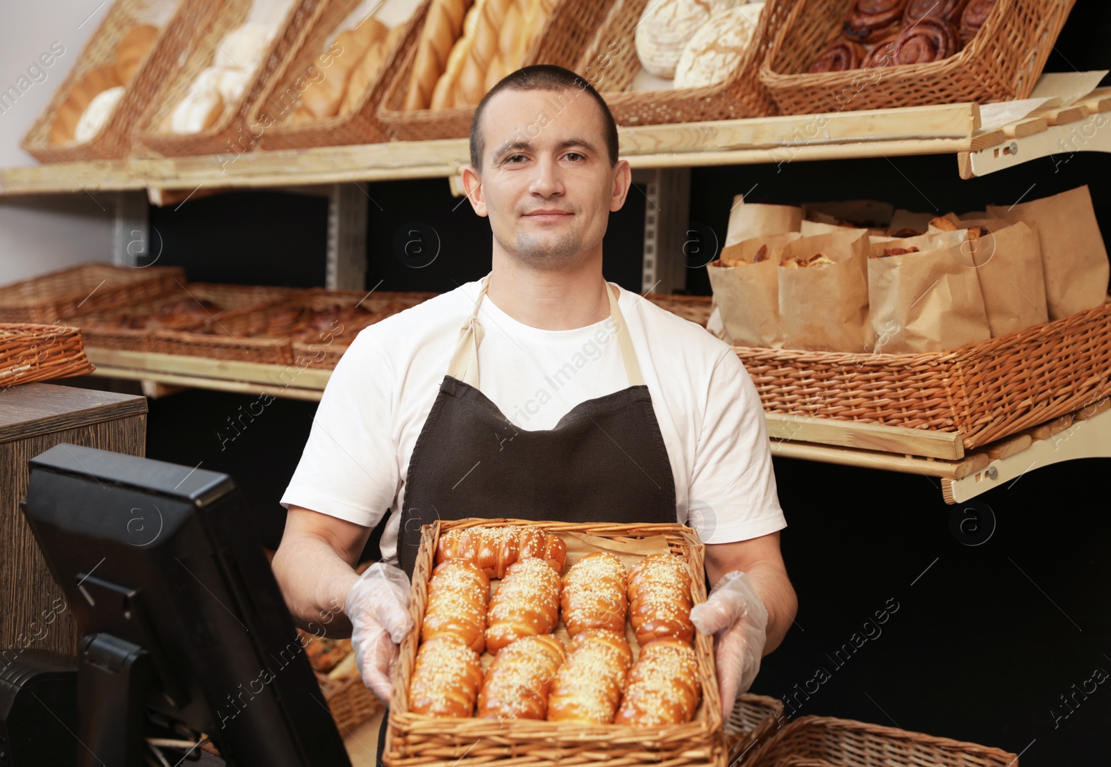 Photo of Portrait of professional baker holding tray with fresh buns near showcase in store