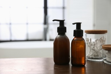 Photo of Dispensers of liquid soap on wooden table in bathroom. Space for text