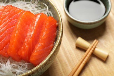 Photo of Delicious salmon sashimi served with funchosa and soy sauce on wooden table, closeup