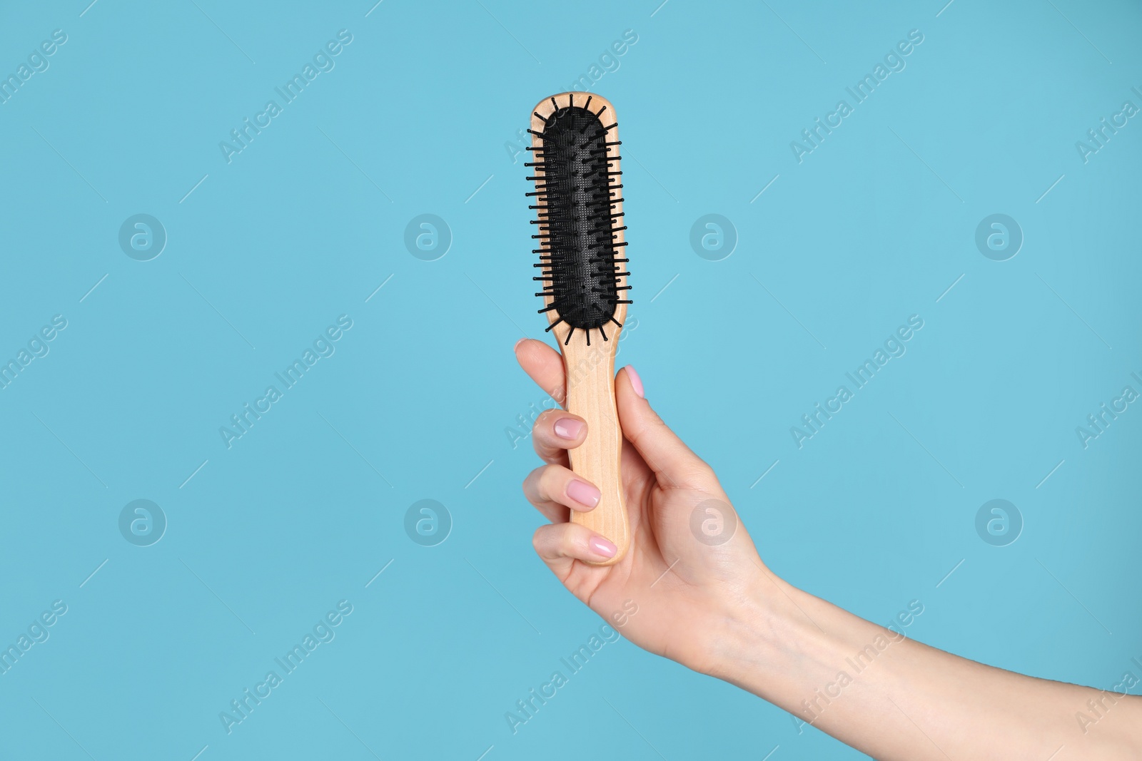 Photo of Woman holding wooden hair brush against blue background, closeup. Space for text