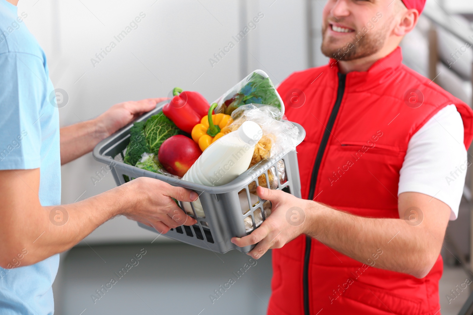 Photo of Courier giving plastic crate with products to customer at home, closeup. Food delivery service