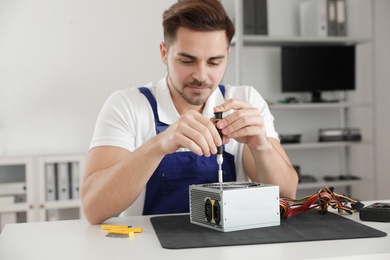 Photo of Male technician repairing power supply unit at table indoors