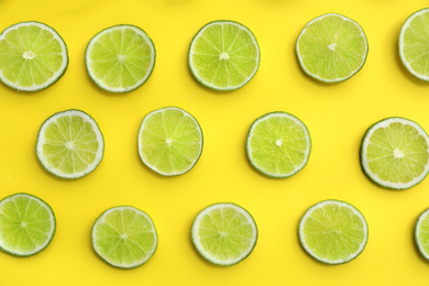 Photo of Slices of fresh juicy limes on yellow background, flat lay