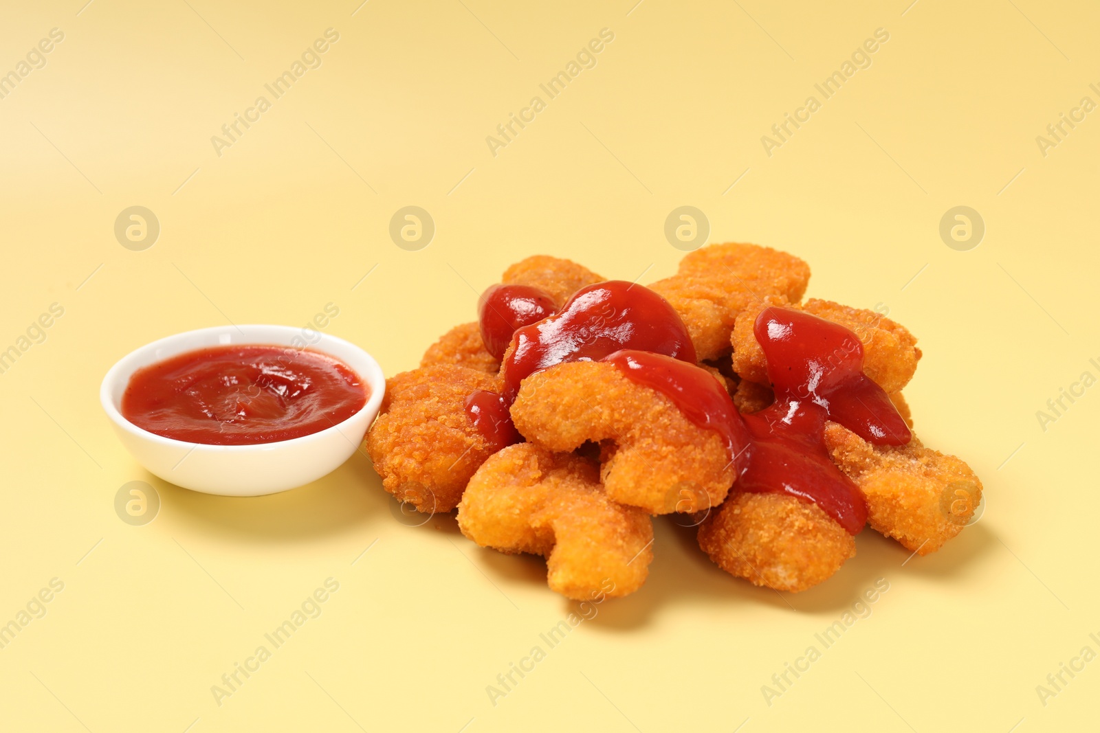 Photo of Tasty chicken nuggets with ketchup on pale yellow background
