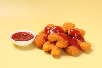 Tasty chicken nuggets with ketchup on pale yellow background