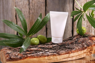 Photo of Tube of cream, olives and leaves on log near wooden wall