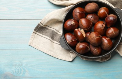 Fresh edible sweet chestnuts in frying pan on light blue wooden table, top view. Space for text