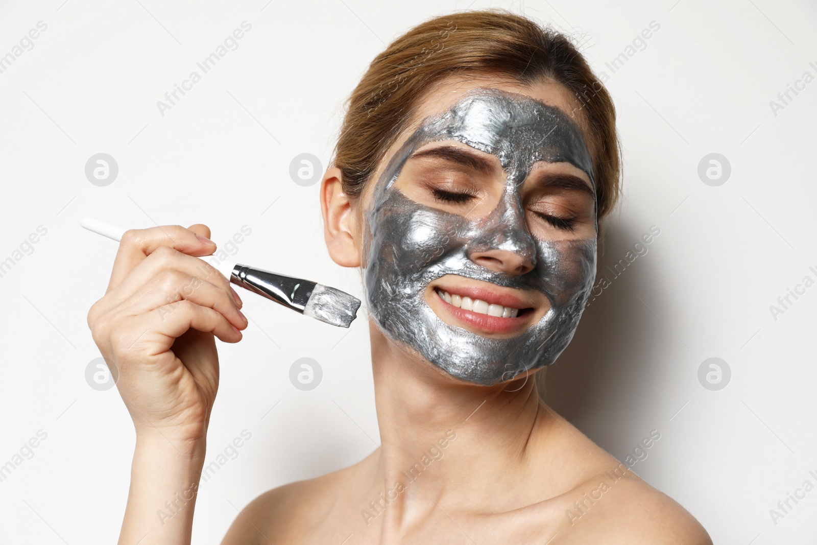 Photo of Beautiful woman applying mask onto face against light background