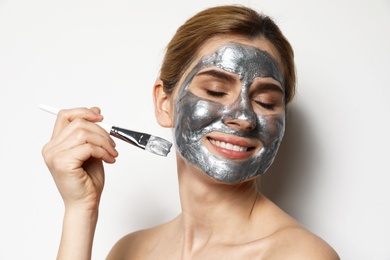 Photo of Beautiful woman applying mask onto face against light background